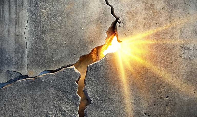 Broken cement wall with glowing light in crack