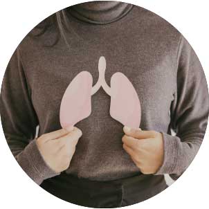Person in a brown sweater holding a paper cutout of human lungs in front of their chest
