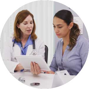 A doctor in a white lab coat shows a tablet screen to a female patient.