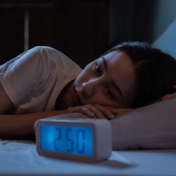 A woman looks at the time on a clock as she lays in bed