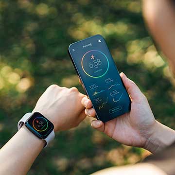 A person wears a fitness watch and holds a phone with fitness stats on it