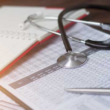 A stethoscope lays on top of a notebook and papers